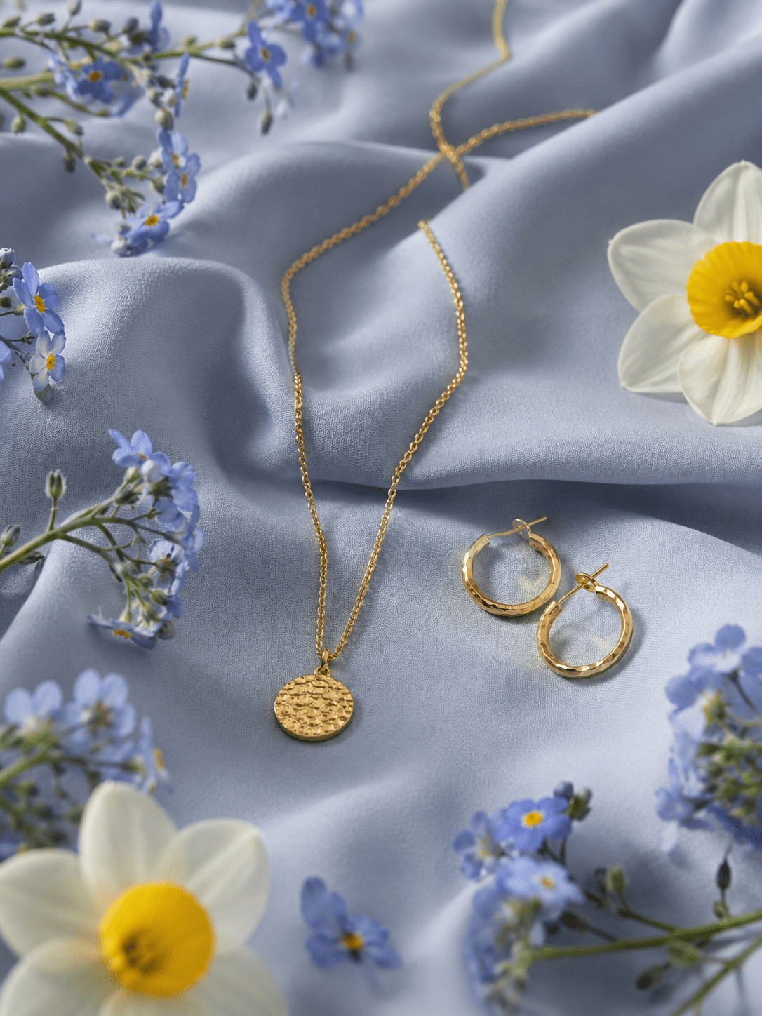 Produktbild Schmuck Flatlay, Goldkette und Ohrringe auf hellblauem Seidenstoff mit Frühlingsblumen